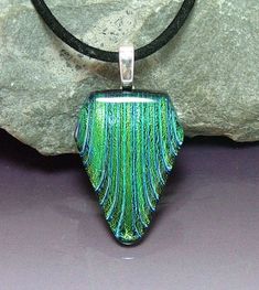 a green and black glass pendant sitting on top of a rock