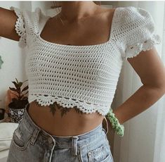 a woman wearing a white crochet crop top and denim shorts with her hands on her hips