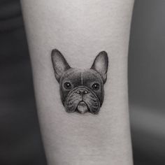 a small black and white dog tattoo on the left inner arm, with an outline of a bulldog's head