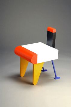 a small table and chair made out of colored paper on a gray background with an orange, black, and white color scheme