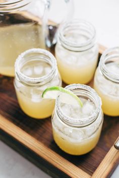 four mason jars filled with lemonade sit on a cutting board next to a spoon