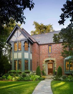 a large brick house with lots of windows and green grass on the front lawn, surrounded by trees