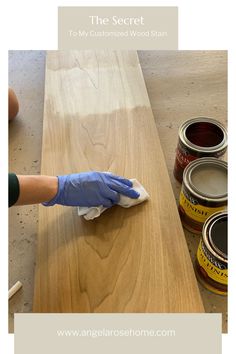 a person in blue gloves is wiping down some paint on a wooden table with two cans