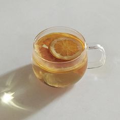 a glass mug filled with liquid and sliced oranges on the rim, sitting on a white surface