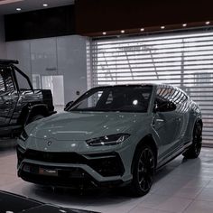 two cars are parked in a showroom, one is gray and the other is black