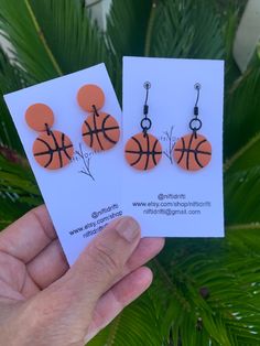 two earrings with basketballs on them are being held in front of a palm tree