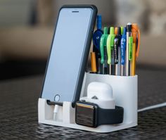 a cell phone holder with pens and pencils in it on a table next to an iphone