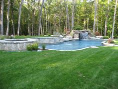 an outdoor pool surrounded by lush green grass and trees, with a waterfall in the middle