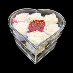 a clear heart shaped box filled with white roses and a red ribbon on the top