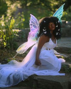 a woman dressed as a fairy sitting on some rocks