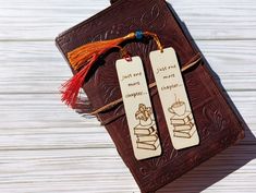 two wooden bookmarks with tassels and writing on them sitting next to each other