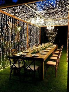 an outdoor dining area is lit up with string lights and greenery to create a backdrop for the dinner table