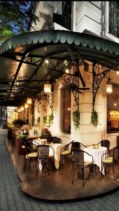 an outdoor dining area with tables and chairs on the side of the building at night