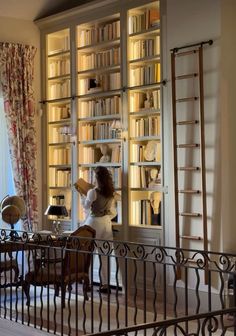 a woman standing in front of a book shelf filled with lots of books next to a window