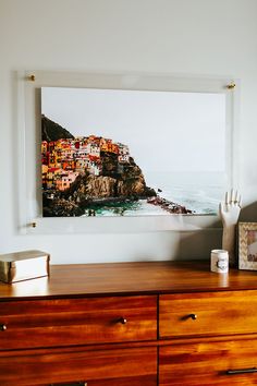 a dresser with a painting hanging on the wall next to it's wooden drawers