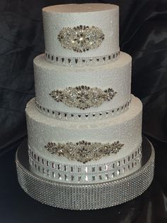 a three tiered white wedding cake with crystal trimmings on the top and sides