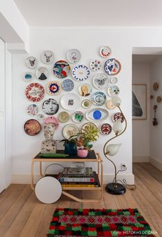 a white room with plates on the wall and a table in front of it that has a lamp next to it