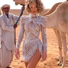 a woman in a silver dress standing next to a man with a camel behind her