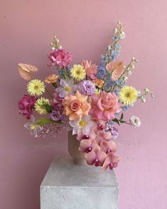 a vase filled with lots of colorful flowers on top of a cement block in front of a pink wall