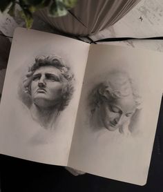 an open book with two drawings of people's faces on it and a plant in the background