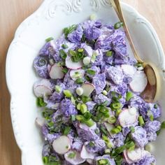 a white bowl filled with purple and green vegetables on top of a wooden table next to a spoon