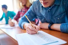 a person writing on a piece of paper with a pencil in their hand and another person behind them