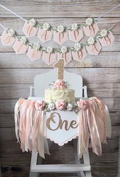 a one year old birthday cake sitting on top of a chair with pink and gold decorations