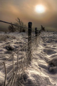 the fence is covered in snow as the sun goes down over the horizon behind it