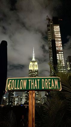 a green street sign sitting in front of a tall building with the words follow that dream on it