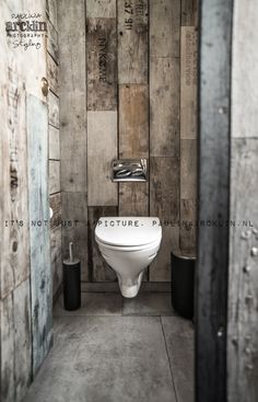 a white toilet sitting in the middle of a bathroom next to a wooden wall with writing on it