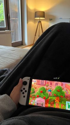 a person holding a nintendo wii game controller in their hand while sitting on a bed