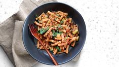 a blue bowl filled with pasta and spinach on top of a napkin next to a fork