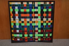 an art piece is displayed in front of a wooden wall with a black frame and multicolored squares on it