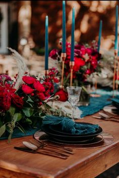 the table is set with red flowers and blue napkins, silverware, and candles