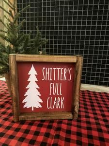 a wooden sign that says shitter's full clark on the table next to a christmas tree