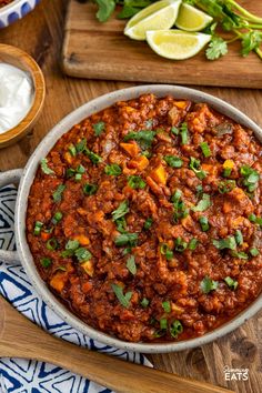 a bowl filled with chili and cilantro on top of a wooden cutting board