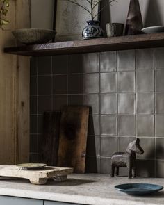 a small toy horse on a counter in a kitchen with grey tiles and wooden shelves