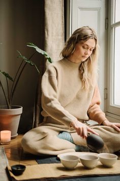 a woman sitting on the floor in front of a window while holding her hands out