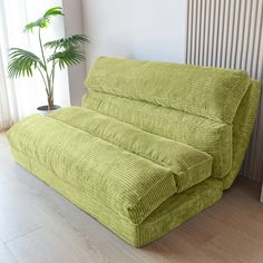 a large green couch sitting on top of a hard wood floor next to a potted plant