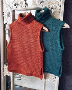 two knitted vests hanging on a mirror