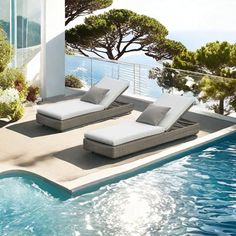 two lounge chairs sitting on the edge of a swimming pool next to an ocean view