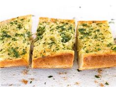 four pieces of bread with herbs on top sitting on a white surface, cut into squares