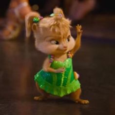 a small toy squirrel is wearing a green dress and has her hand up in the air