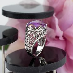 "Indulge in the allure of our Handcrafted Sterling Silver Dome Cocktail Ring, a masterpiece of filigree artistry. Meticulously handcrafted from 925 sterling silver, this statement ring features a captivating 13x18 mm cabochon or faceted oval cut gemstone, available in the natural, soothing Rhodonite, the vibrant Purple Mohave Turquoise, or the regal Amethyst. The ring face length is 0.80 inches and the width is 0.60 inches  Each gemstone holds its unique charm: Rhodonite, a symbol of compassion and love; Purple Mohave Turquoise, a beacon of creativity and protection; and Amethyst, a stone of clarity and spirituality. Our commitment to impeccable craftsmanship extends to fit, with 16 different sizes ranging from a dainty size 5 to a luxurious 12.5, including half sizes. Searching for the pe Spiritual Open Ring Jewelry For Formal Occasions, Silver Opal Ring With Accent Stones For Gift, Elegant Amethyst Cabochon Ring, Fine Jewelry Purple Cabochon, Elegant Collectible Cabochon Turquoise Ring, Purple Opal Ring Gift, Unique Opal Ring With Accent Stones As Gift, Bohemian Oval Jewelry With Accent Stones, Fine Jewelry Amethyst Cabochon