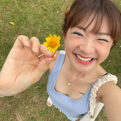 a woman holding a yellow flower in her right hand and smiling at the camera while laying on the grass