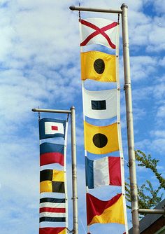 three flags are flying in the wind on a sunny day with blue sky and clouds