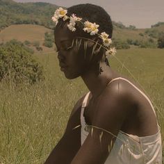 a woman with flowers in her hair sits on the grass and looks off into the distance