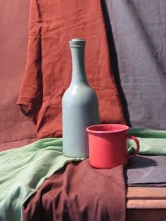 a bottle and cup sitting on top of a wooden table next to a red cloth