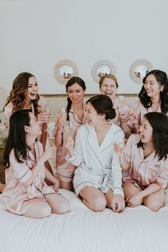 a group of women sitting on top of a bed holding wine glasses in their hands