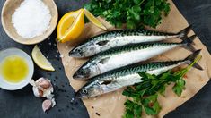 three fish are sitting on a cutting board next to some lemons and parsley